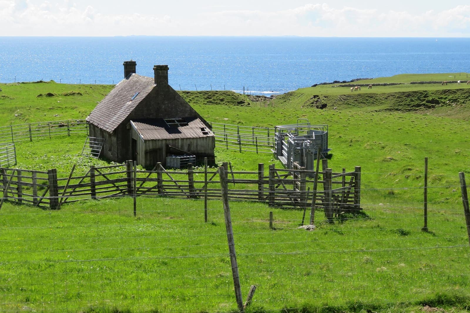 Small stone cottage among wooden fences in a green pasture above the sea
