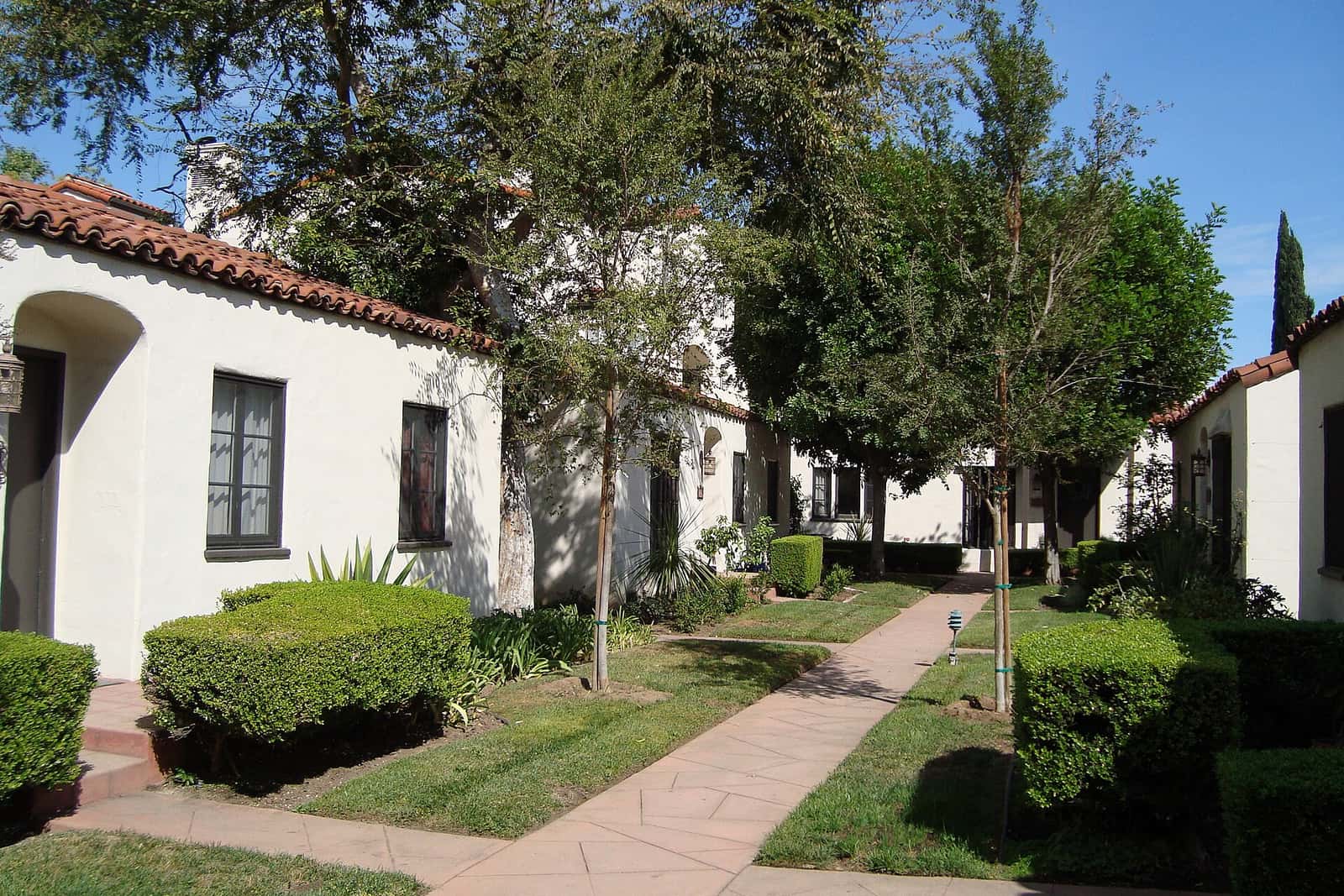 Row of small white stucco cottages with tile roofs around a landscaped garden walkway
