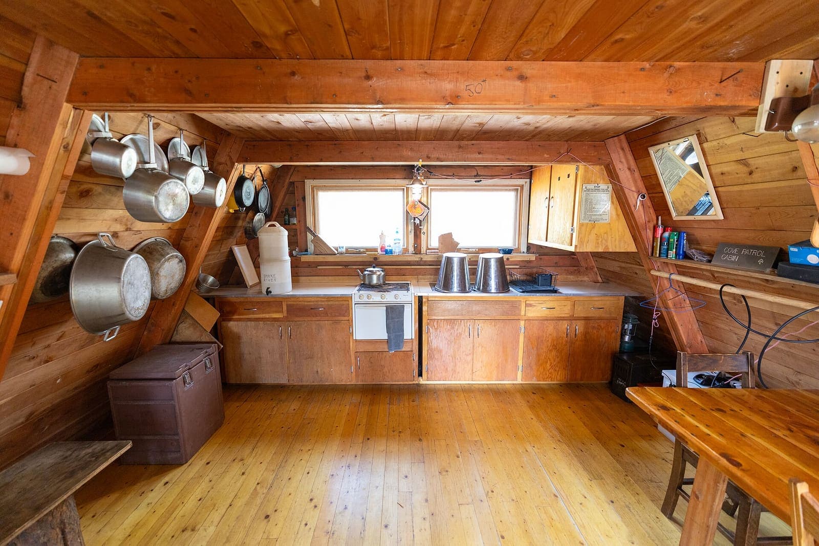 Compact cabin kitchen with pine walls, wooden cabinets, hanging pots and a wood floor