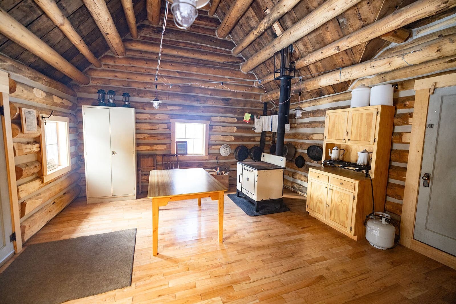 Log cabin interior with a dining table, cookstove and pine cupboards