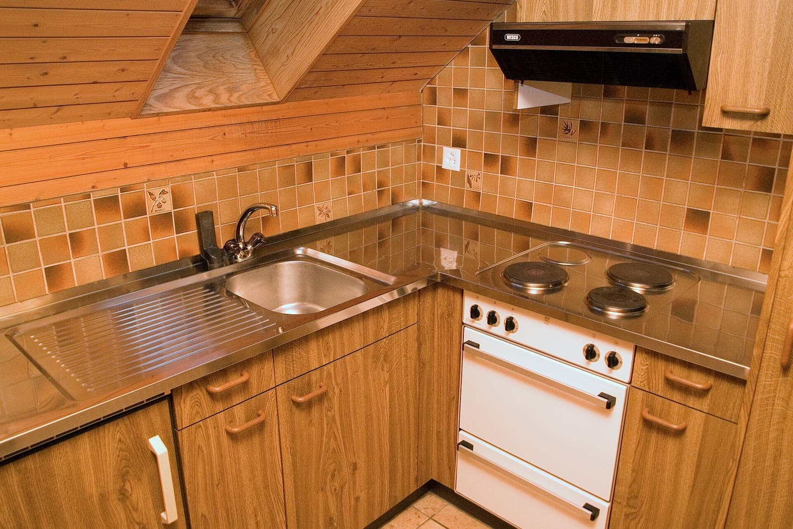 Compact L-shaped kitchen with wood cabinetry under a sloped attic ceiling