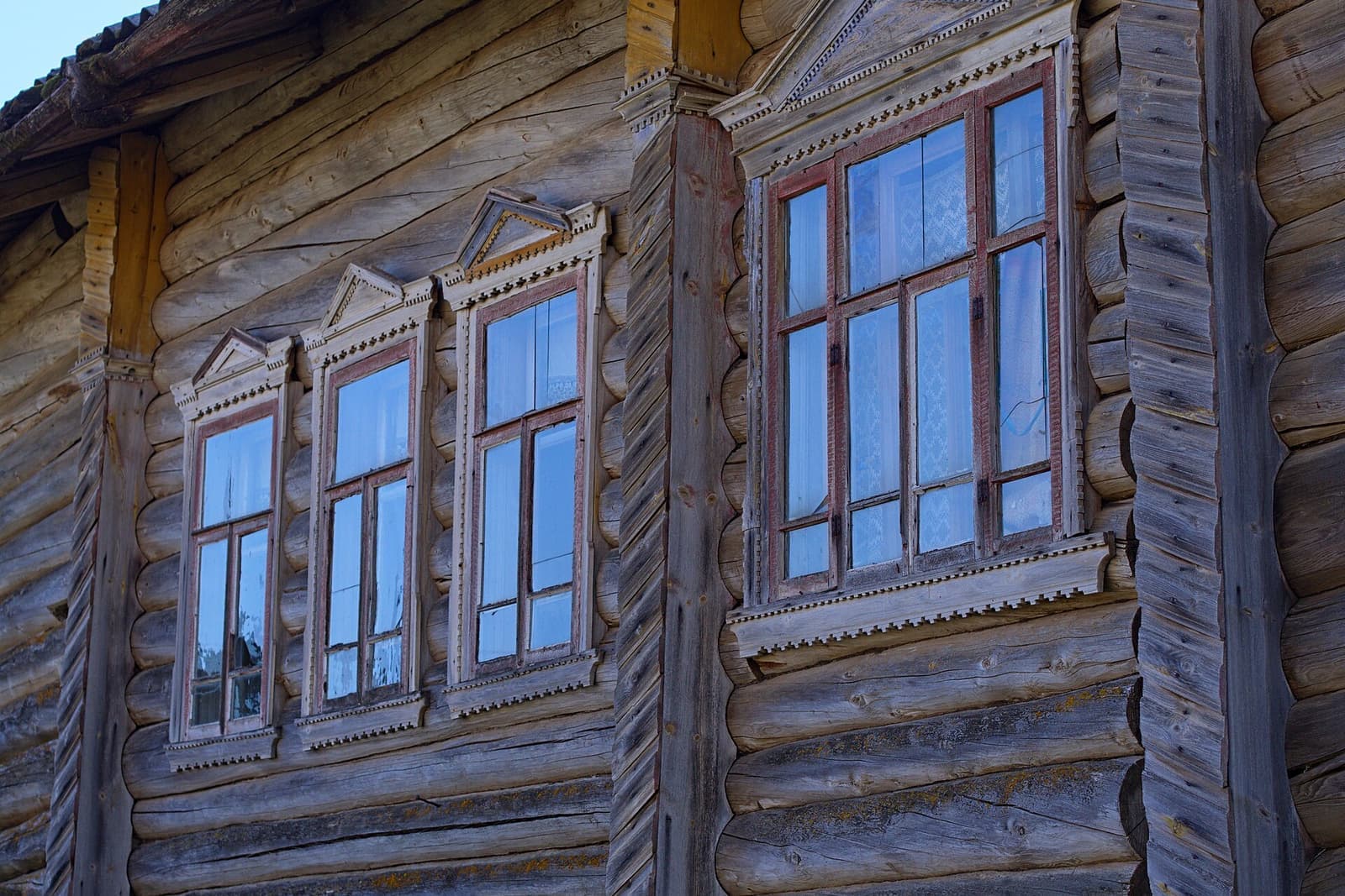 Tall multi-pane windows with carved wooden trim on a weathered log house