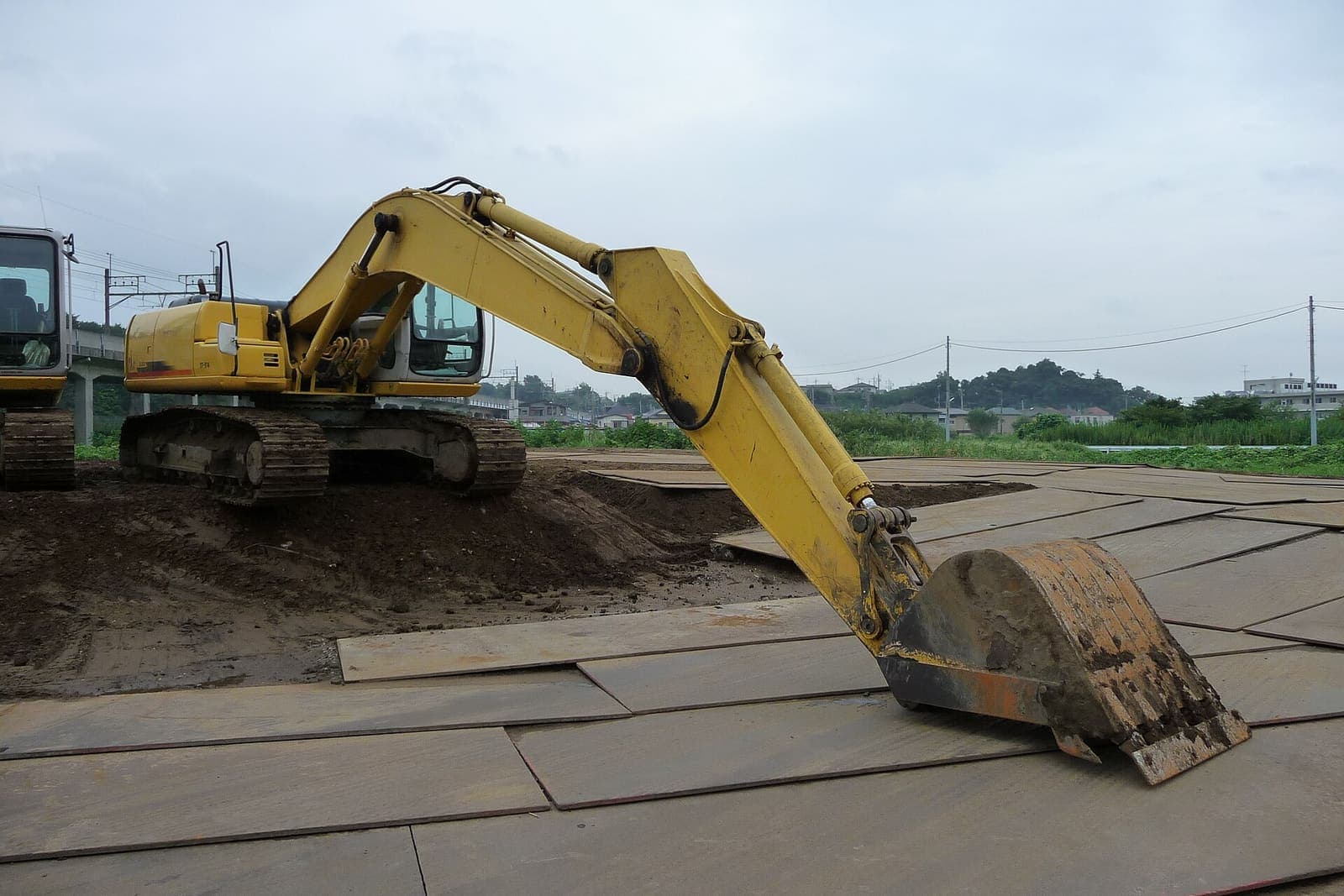 Yellow excavator digging on a site covered with steel road plates