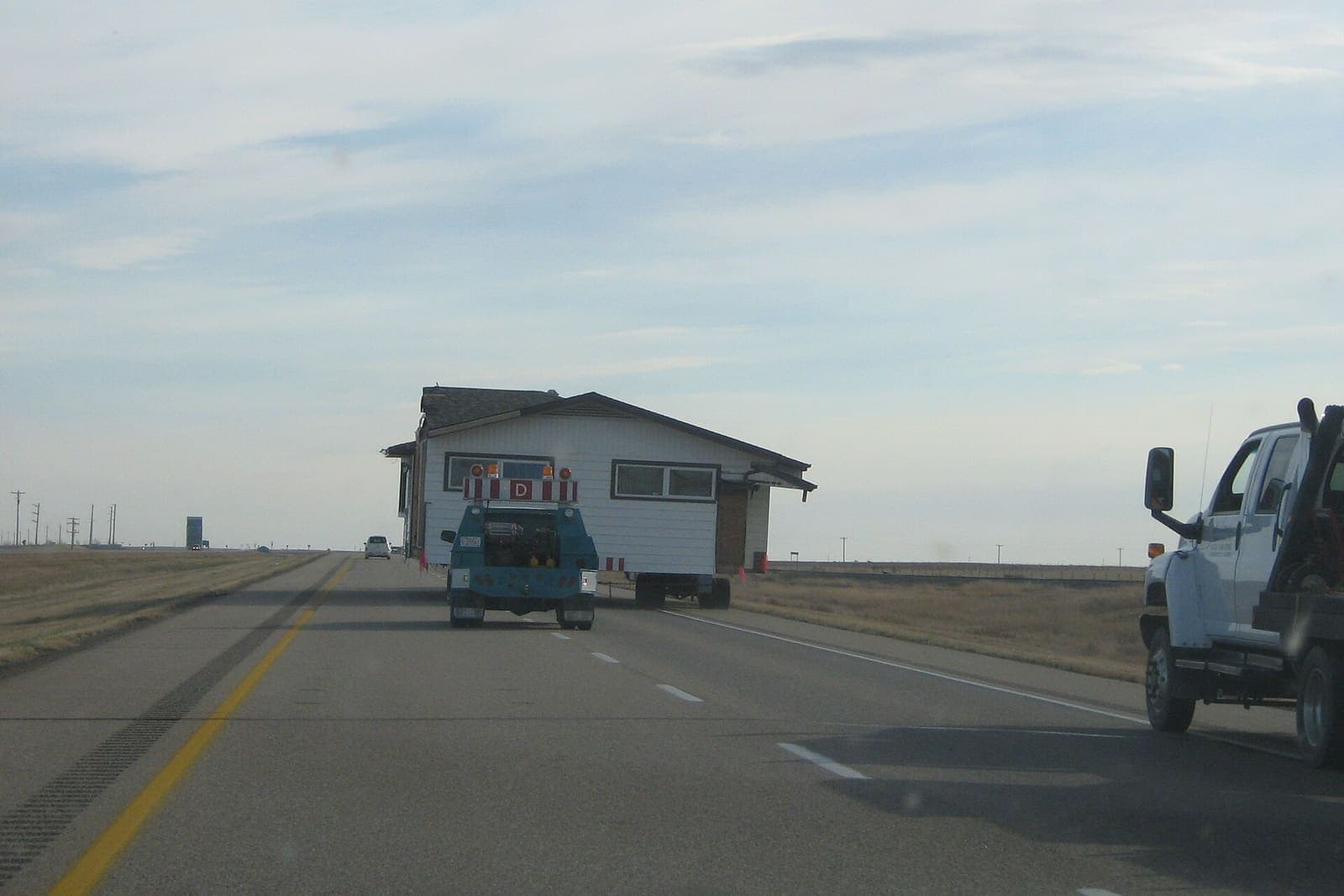Small house being hauled down a prairie highway on a transport trailer